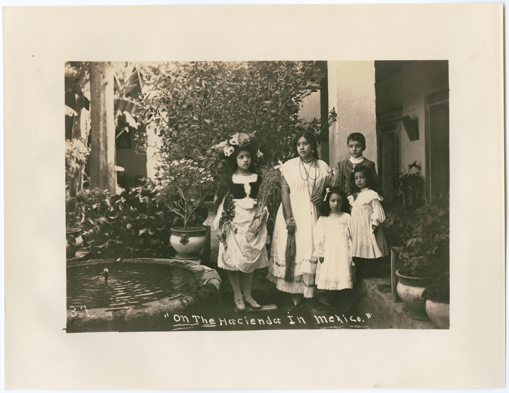 A woman and four children in white dresses posed in a garden courtyard on a hacienda